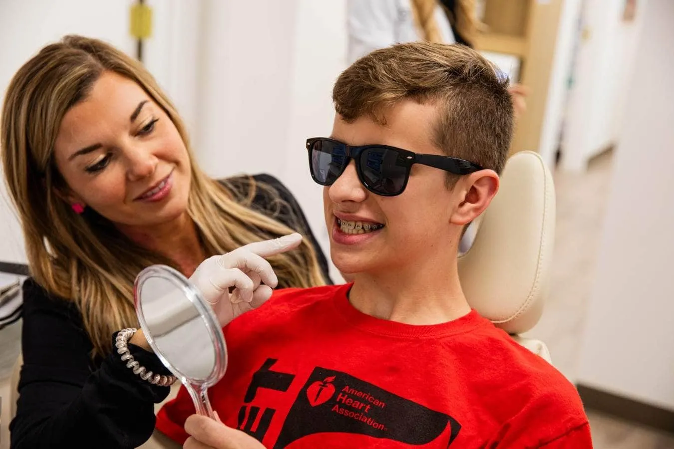 Orthodontist chatting with a smiling teen in sunglasses who has braces