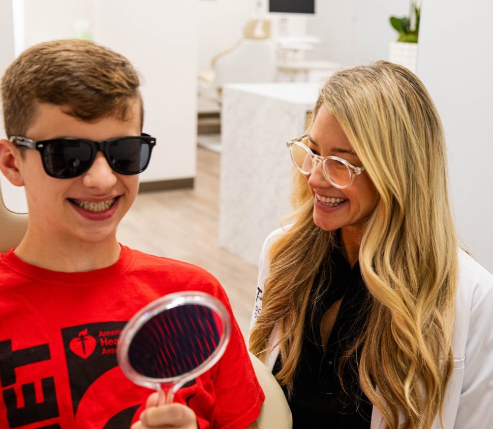 A happy teenager inspecting his newly treated braces in the mirror at Otto Orthodontics. He smiles with excitement, showcasing the successful completion of his orthodontic treatment. The braces are neatly aligned, reflecting the expertise of Otto Orthodontics in achieving a confident and healthy smile for their young patients.